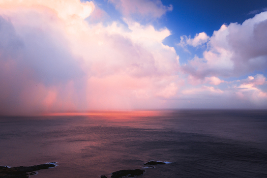 Aerial view of the vast dark blue sea reflecting the fiery sunset beneath a blanket of pink tinged clouds Reinebringen Nordland Norway.