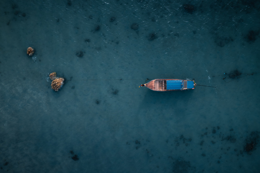 Aerial view of a traditional long tail boat floating in the clear turquoise waters of Pi Leh Bay with rocky outcrops visible beneath the surface in Tambon Ao Nang Chang Wat Krabi Thailand. Aerial view of a traditional long tail boat floating in the clear turquoise waters of Pi Leh Bay with rocky outcrops visible beneath the surface in Tambon Ao Nang Chang Wat Krabi Thailand.