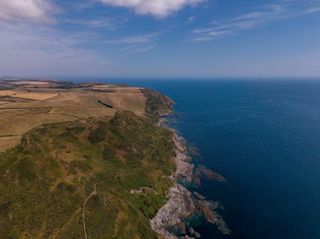 Aerial view of the rugged coastline and green fields of Lansallos meeting the deep blue sea in Lansallos England United Kingdom. Aerial view of the rugged coastline and green fields of Lansallos meeting the deep blue sea in Lansallos England United Kingdom.