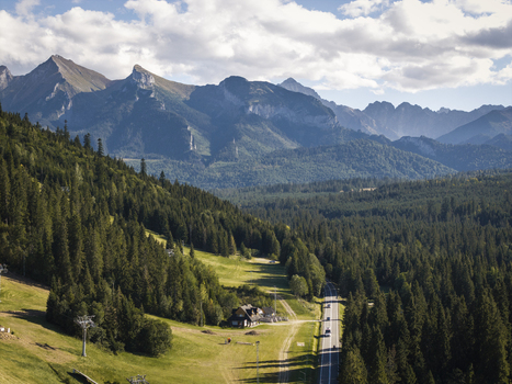 Aerial view of the Tatra Mountains landscape in Jurgow featuring a dense pine forest a winding road and grassy slopes under a partly cloudy sky in Jurgow Lesser Poland Voivode Poland. Aerial view of the Tatra Mountains landscape in Jurgow featuring a dense pine forest a winding road and grassy slopes under a partly cloudy sky in Jurgow Lesser Poland Voivode Poland.