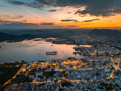 Aerial view of the illuminated City Palace and Lake Pichola at sunset with the surrounding urban landscape of Udaipur Rajasthan India.