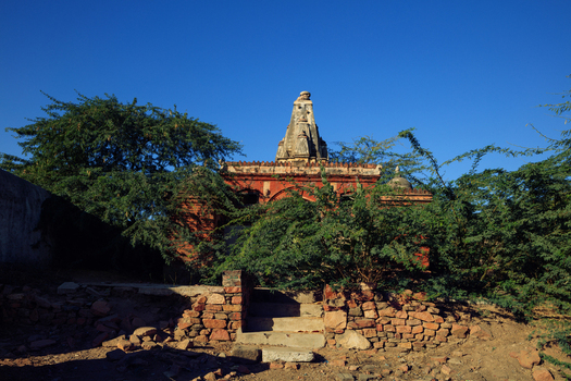 View of the abandoned temple at Nagarparkar featuring a weathered stone structure partially obscured by green trees and shrubs set against a clear blue sky in Nagarparkar Sindh Pakistan.