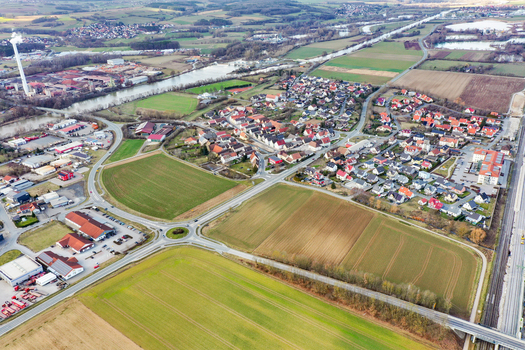Aerial view of the town of Buttenheim featuring residential houses industrial buildings with a tall chimney and green agricultural fields in Buttenheim Bavaria Germany. Aerial view of the town of Buttenheim featuring residential houses industrial buildings with a tall chimney and green agricultural fields in Buttenheim Bavaria Germany.