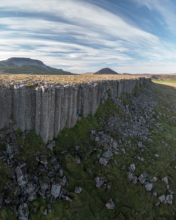 Aerial view of Gerduberg Cliffs featuring massive basalt columns rising above the green landscape under a blue sky with wispy clouds in Raudhamelur Eyja og Miklaholtshr Iceland. Aerial view of Gerduberg Cliffs featuring massive basalt columns rising above the green landscape under a blue sky with wispy clouds in Raudhamelur Eyja og Miklaholtshr Iceland.