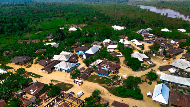 Aerial view of the village of Abua featuring traditional houses with metal roofs dirt roads and lush tropical vegetation near a river in Abua Rivers Nigeria. Aerial view of the village of Abua featuring traditional houses with metal roofs dirt roads and lush tropical vegetation near a river in Abua Rivers Nigeria.