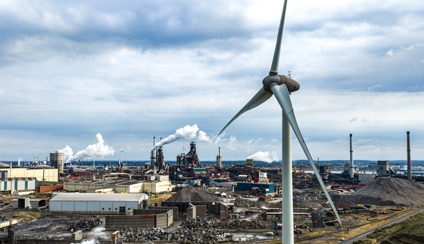 Aerial view of the Tata Steel industrial complex with a large wind turbine in the foreground smokestacks and factory buildings under a cloudy sky in Velsen Noord Noord Holland Netherlands. Aerial view of the Tata Steel industrial complex with a large wind turbine in the foreground smokestacks and factory buildings under a cloudy sky in Velsen Noord Noord Holland Netherlands.