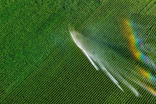 Aerial view of a center pivot irrigation system watering a lush green corn field with a vibrant rainbow visible in the mist in Hombourg Grand Est France. Aerial view of a center pivot irrigation system watering a lush green corn field with a vibrant rainbow visible in the mist in Hombourg Grand Est France.