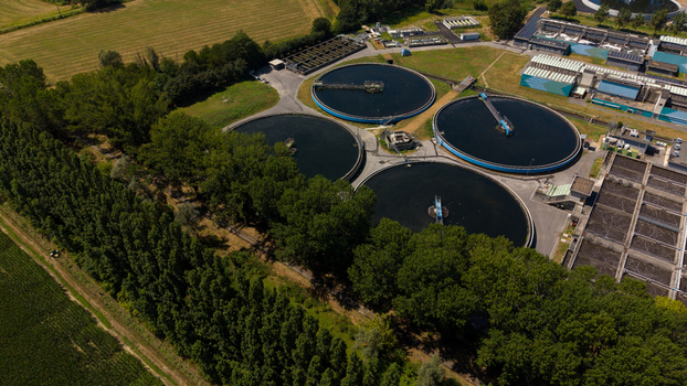 Aerial view of a wastewater treatment plant with circular sedimentation tanks surrounded by lush trees and agricultural fields in Milan Lombardy Italy. Aerial view of a wastewater treatment plant with circular sedimentation tanks surrounded by lush trees and agricultural fields in Milan Lombardy Italy.
