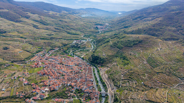 Aerial view of the town nestled in a valley with terracotta rooftops contrasting with the green slopes and a river cutting through Cabezuela del Valle Extremadura Spain.
