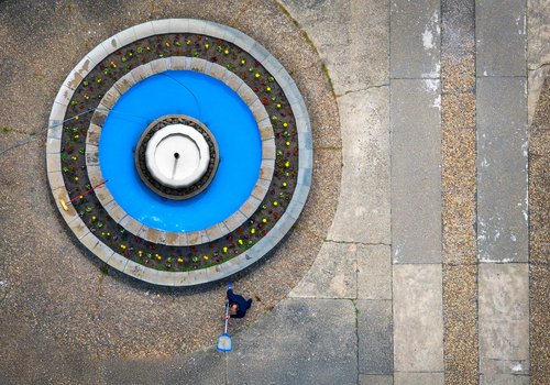 Aerial view of a worker cleaning a circular fountain with blue water and surrounding flowers in a public square in Belgrade City of Belgrade Serbia. Aerial view of a worker cleaning a circular fountain with blue water and surrounding flowers in a public square in Belgrade City of Belgrade Serbia.