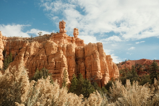 View of the iconic red rock hoodoos and sandstone cliffs of Bryce Canyon National Park surrounded by green pine trees under a blue sky Utah United States. View of the iconic red rock hoodoos and sandstone cliffs of Bryce Canyon National Park surrounded by green pine trees under a blue sky Utah United States.