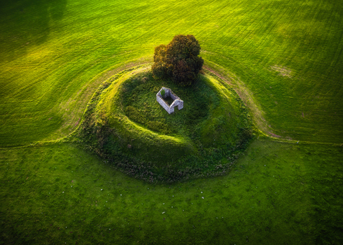 Aerial view of a ruined stone building situated within a circular green ringfort surrounded by lush pastures at sunset in Mosstown County Meath Ireland.