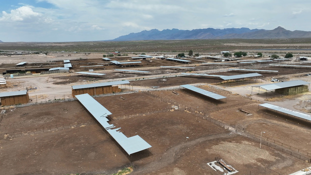 Aerial view of Las Cruces cattle feedlot with rows of metal shelters dry pens and distant mountains under a blue sky in Las Cruces New Mexico United States. Aerial view of Las Cruces cattle feedlot with rows of metal shelters dry pens and distant mountains under a blue sky in Las Cruces New Mexico United States.