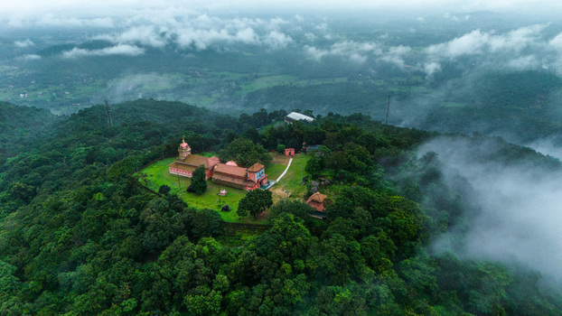 Aerial view of Shri Chandreshwar Bhootnath Temple on a lush green hilltop surrounded by mist and clouds in Paroda Goa India.