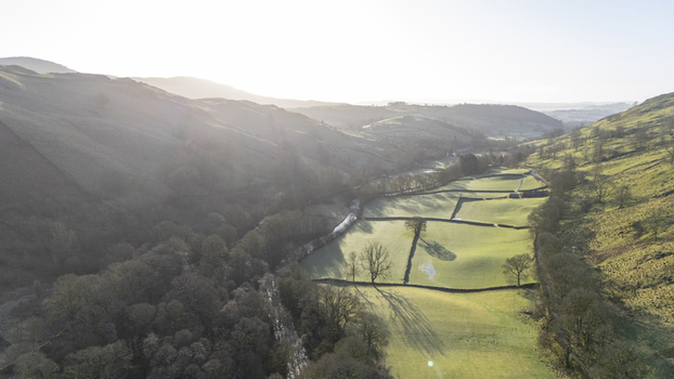 Aerial view of sun kissed meadows nestled between rolling hills divided by stone walls creating a tapestry of light and shadow Lake District England United Kingdom. Aerial view of sun kissed meadows nestled between rolling hills divided by stone walls creating a tapestry of light and shadow Lake District England United Kingdom.