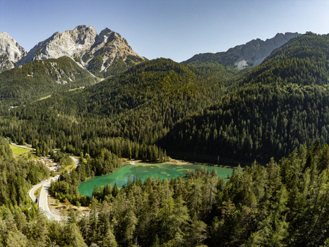 Aerial view of Mittersee surrounded by dense pine forests and rugged alpine mountains under a clear blue sky in Biberwier Tirol Austria.