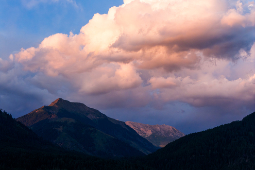 Aerial view of Fiemme Valley with dramatic sunset clouds illuminating the mountain peaks and dense pine forests in Trentino Alto Adige Italy.