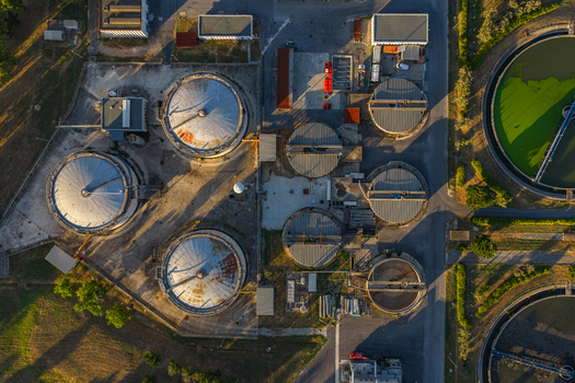 Aerial view of a water treatment plant featuring large circular sedimentation tanks and industrial infrastructure surrounded by green landscape in Rome Lazio Italy.