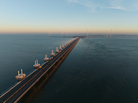 Aerial view of the Deltawerken storm surge barrier with wind turbines and a road over the sea during sunset in the Netherlands.