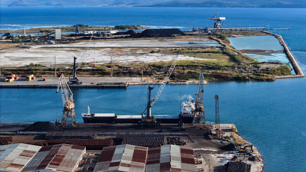 Aerial view of Port of Ploce with a cargo ship docked at the industrial terminal featuring large cranes stockpiles of bulk materials and warehouses along the coastline in Croatia. Aerial view of Port of Ploce with a cargo ship docked at the industrial terminal featuring large cranes stockpiles of bulk materials and warehouses along the coastline in Croatia.