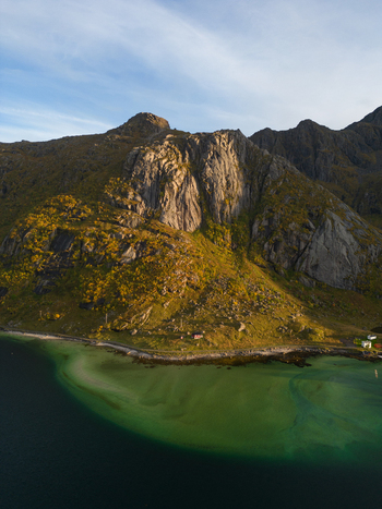Aerial view of the rugged mountains and clear turquoise waters of Tangstad with autumn foliage and a coastal road in Leknes Nordland Norway. Aerial view of the rugged mountains and clear turquoise waters of Tangstad with autumn foliage and a coastal road in Leknes Nordland Norway.