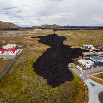 Aerial view of a solidified black lava flow encroaching on residential buildings and infrastructure in a volcanic landscape in Iceland. Aerial view of a solidified black lava flow encroaching on residential buildings and infrastructure in a volcanic landscape in Iceland.