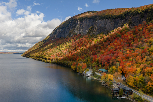 Aerial view of Lake Willoughby surrounded by vibrant autumn foliage on the mountainside with a road and houses along the shoreline in Westmore Vermont United States. Aerial view of Lake Willoughby surrounded by vibrant autumn foliage on the mountainside with a road and houses along the shoreline in Westmore Vermont United States.