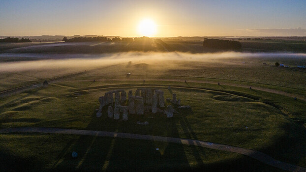 Aerial view of Stonehenge surrounded by morning mist at sunrise with the ancient stone circle casting long shadows across the grassy landscape in Salisbury England United Kingdom. Aerial view of Stonehenge surrounded by morning mist at sunrise with the ancient stone circle casting long shadows across the grassy landscape in Salisbury England United Kingdom.