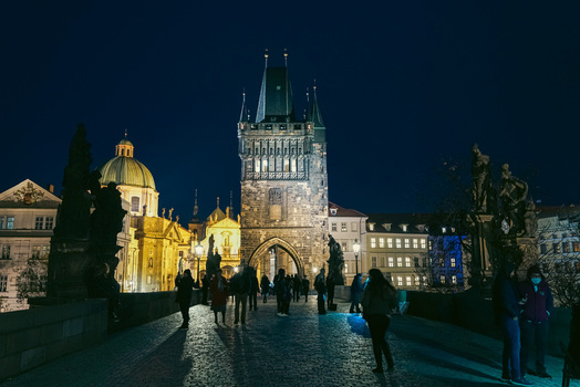 Prague Czechia 03 November 2021 View of the illuminated Old Town Bridge Tower on Charles Bridge at night with people walking on the cobblestone path. Prague Czechia 03 November 2021 View of the illuminated Old Town Bridge Tower on Charles Bridge at night with people walking on the cobblestone path.