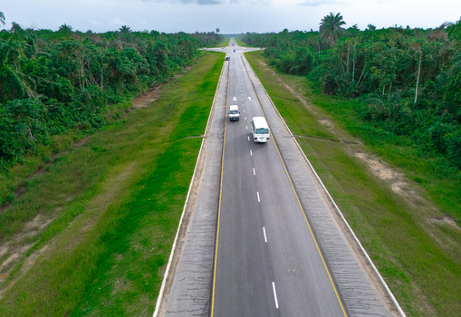 Aerial view of a straight asphalt road cutting through dense green forest on Bonny Island with vehicles driving along the highway Bonny Town Rivers Nigeria. Aerial view of a straight asphalt road cutting through dense green forest on Bonny Island with vehicles driving along the highway Bonny Town Rivers Nigeria.