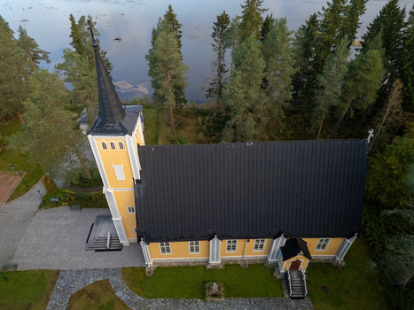 Aerial view of the historic Muhos Church with its yellow wooden walls and dark roof surrounded by pine trees and green lawns in Muhos North Ostrobothnia Finland. Aerial view of the historic Muhos Church with its yellow wooden walls and dark roof surrounded by pine trees and green lawns in Muhos North Ostrobothnia Finland.