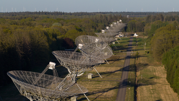 Aerial view of the Westerbork Synthesis Radio Telescope array with large parabolic dishes lined up along a path through a dense forest under a clear sky Zwiggelte Drenthe Netherlands. Aerial view of the Westerbork Synthesis Radio Telescope array with large parabolic dishes lined up along a path through a dense forest under a clear sky Zwiggelte Drenthe Netherlands.