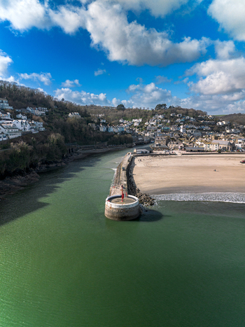 Aerial view of Banjo Pier extending into the sea with the coastal town of Looe sandy beach and rolling hills in the background under a blue sky in Looe Cornwall United Kingdom. Aerial view of Banjo Pier extending into the sea with the coastal town of Looe sandy beach and rolling hills in the background under a blue sky in Looe Cornwall United Kingdom.