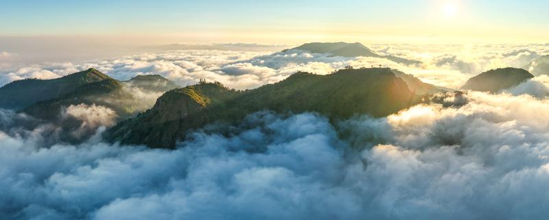 Aerial view of Dieng Plateau with green mountain peaks rising above a thick sea of clouds during golden hour in Indonesia.