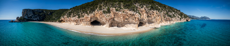 Aerial view of Cala Luna beach featuring its iconic sea caves white sand and turquoise waters along the rugged limestone coastline of Baunei Sardegna Italy. Aerial view of Cala Luna beach featuring its iconic sea caves white sand and turquoise waters along the rugged limestone coastline of Baunei Sardegna Italy.