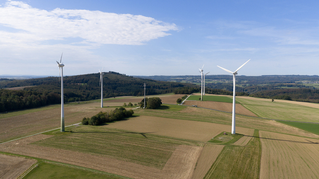 Aerial view of Windpark Eppenrod featuring several wind turbines standing amidst agricultural fields and rolling hills under a clear blue sky in Eppenrod Rheinland Pfalz Germany.