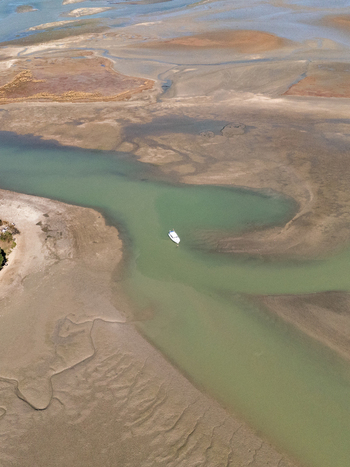 Aerial view of a boat sailing through the winding waterway its wake a stark contrast against the muddy banks Abel Tasman Tasman Region New Zealand. Aerial view of a boat sailing through the winding waterway its wake a stark contrast against the muddy banks Abel Tasman Tasman Region New Zealand.