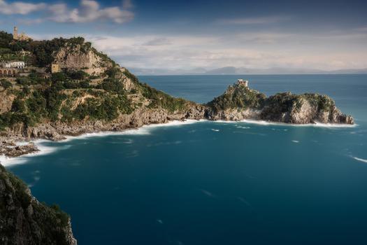 View of steep green cliffs meeting the deep blue sea white waves churn below ancient towers Conca dei Marini Campania Italy. View of steep green cliffs meeting the deep blue sea white waves churn below ancient towers Conca dei Marini Campania Italy.