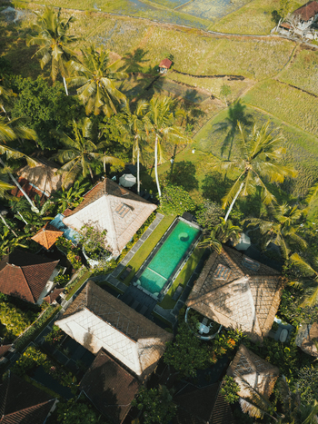 Aerial view of a luxury villa with a swimming pool surrounded by lush palm trees and rice fields in Ubud Bali Indonesia. Aerial view of a luxury villa with a swimming pool surrounded by lush palm trees and rice fields in Ubud Bali Indonesia.