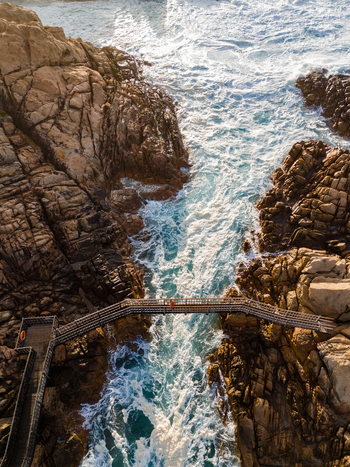 Aerial view of the Canal Rocks Bridge crossing over turbulent ocean waves between rugged granite cliffs in Yallingup Western Australia Australia. Aerial view of the Canal Rocks Bridge crossing over turbulent ocean waves between rugged granite cliffs in Yallingup Western Australia Australia.