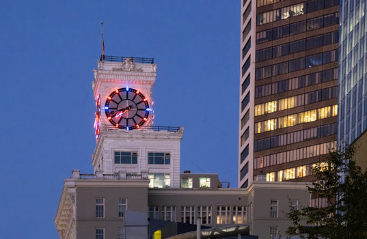 View of the illuminated Vancouver Block clock tower with red and blue neon lights against a twilight sky and modern skyscrapers in Vancouver British Columbia Canada.