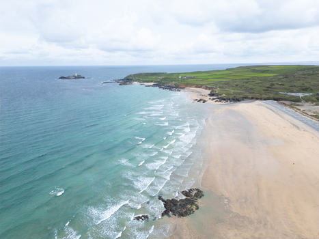 Aerial view of Godrevy Beach with turquoise waves crashing on the sandy shore green coastal fields and a lighthouse on a rocky island in Gwithian England United Kingdom. Aerial view of Godrevy Beach with turquoise waves crashing on the sandy shore green coastal fields and a lighthouse on a rocky island in Gwithian England United Kingdom.