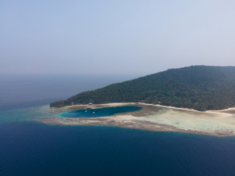 Aerial view of Sorido Bay featuring turquoise waters coral reefs and lush tropical vegetation on the island with a small wooden jetty Raja Ampat Papua Barat Daya Indonesia.