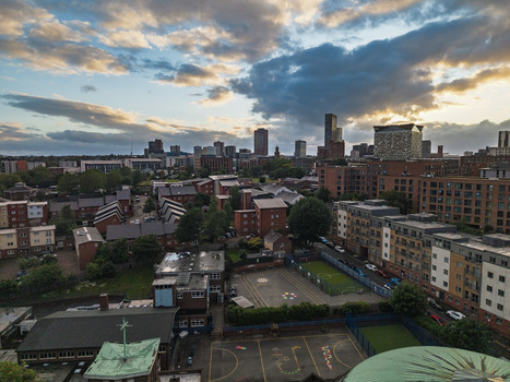 Aerial view of the Birmingham city skyline at sunset featuring modern skyscrapers residential blocks and a school playground under a dramatic cloudy sky in Birmingham England United Kingdom.
