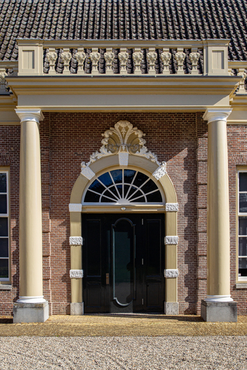 View of the ornate entrance of Castle Groeneveld featuring classic columns a decorative arched doorway and red brick walls Baarn Utrecht Netherlands.