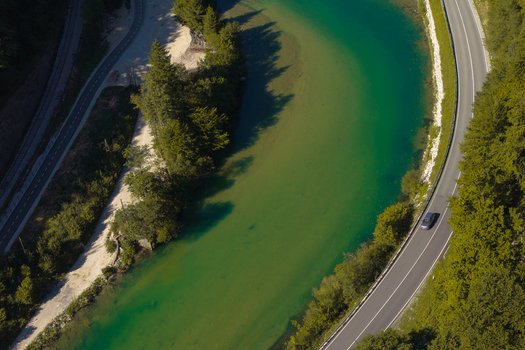 Aerial view of Sava Bohinjka river flowing alongside a winding road with lush green trees in Radovljica Slovenia.