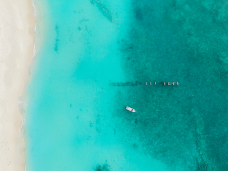Aerial view of white sand beach meeting brilliant turquoise waters a small boat near wooden pilings Hoarafushi Thiladhunmathee Uthuruburi Maldives. Aerial view of white sand beach meeting brilliant turquoise waters a small boat near wooden pilings Hoarafushi Thiladhunmathee Uthuruburi Maldives.