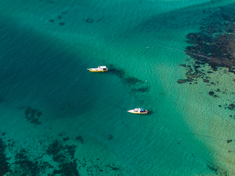 Aerial view of two small boats floating in clear turquoise water over a coral reef in Kecamatan Denpasar Selatan Bali Indonesia.