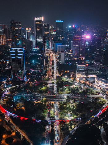 Aerial view of the Semanggi Interchange at night with illuminated skyscrapers busy traffic trails and urban greenery in Jakarta Indonesia.