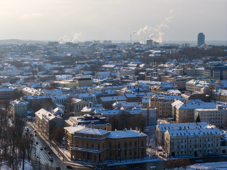 Aerial view of snow covered rooftops and urban architecture under a winter sky with smoke rising from chimneys in the distance Vilnius County Lithuania.